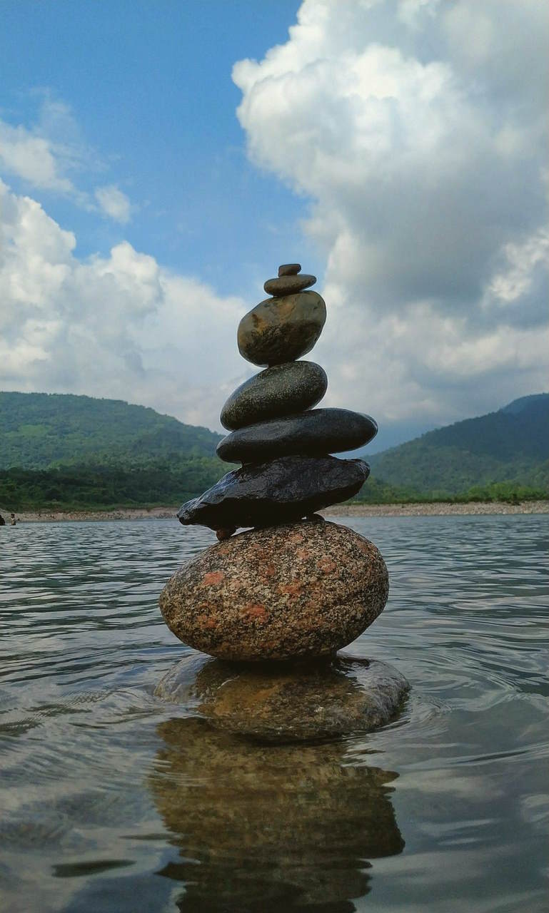 Cairn de pierres en équilibre dans l’eau, devant un paysage de montagnes verdoyantes